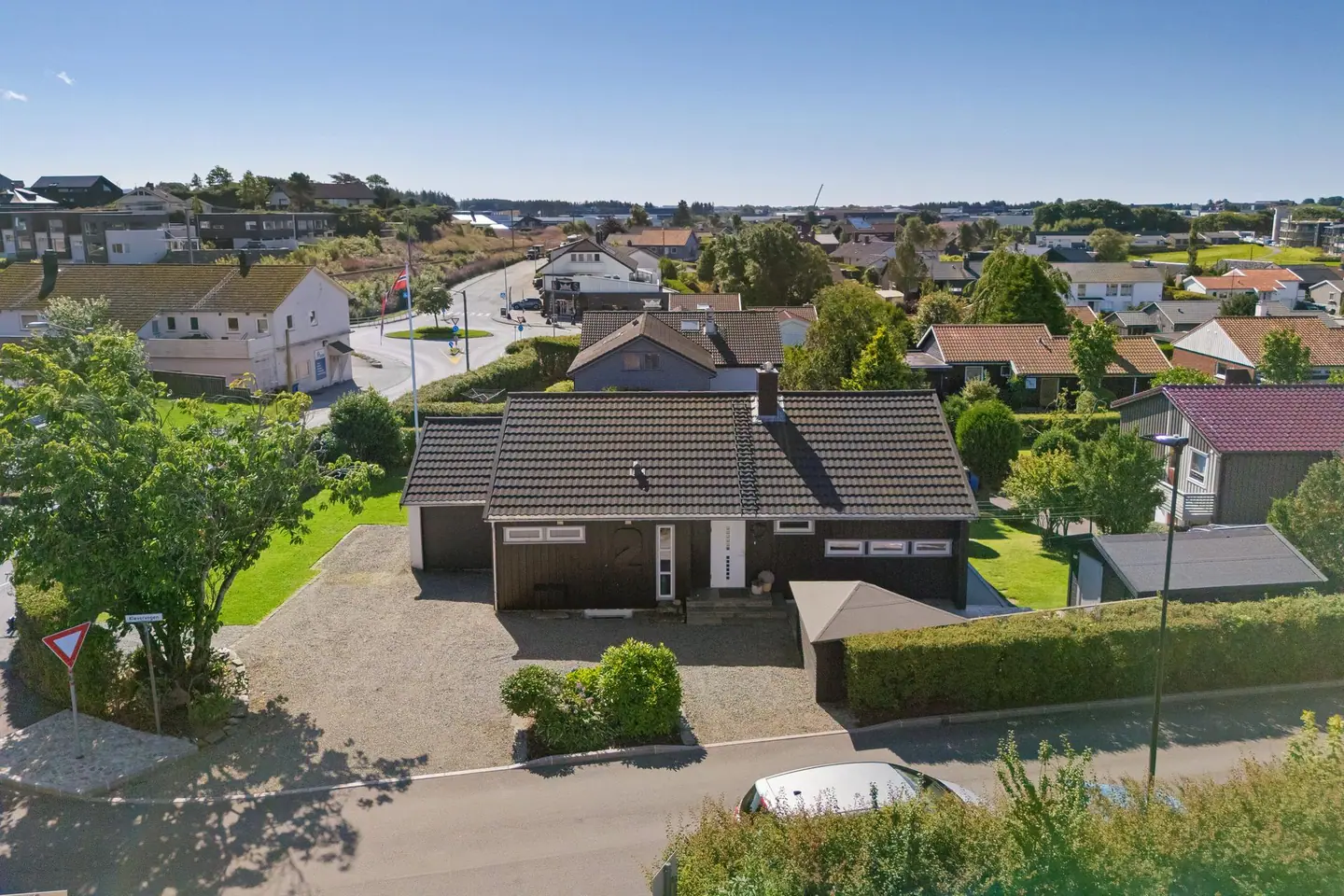 Eiendommen har en oversiktlig tomt med gruset gårdsplass og hekk mot veien.