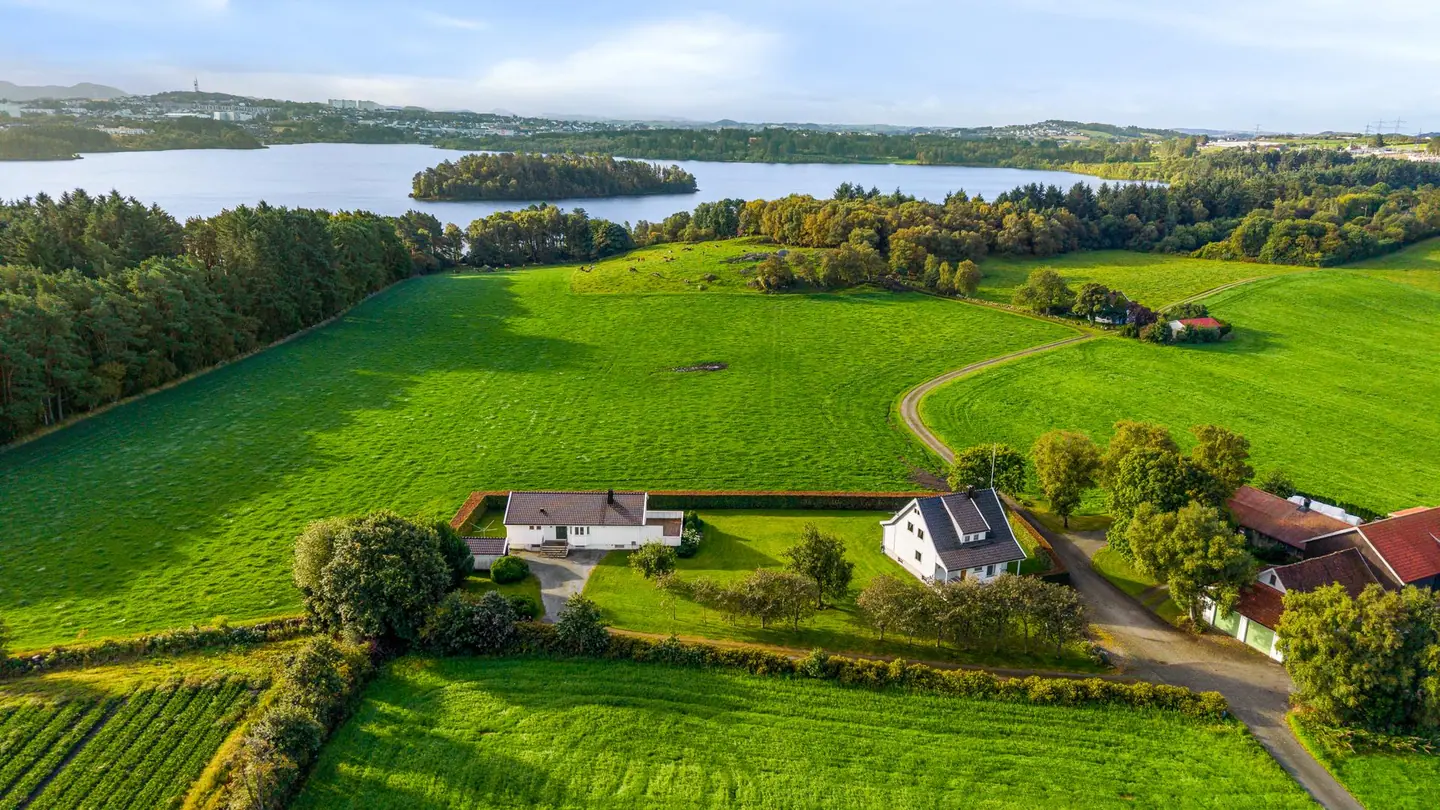 Tunet med de to bolighusene ligger skjermet i det åpne landskapet med utsikt mot vannet.