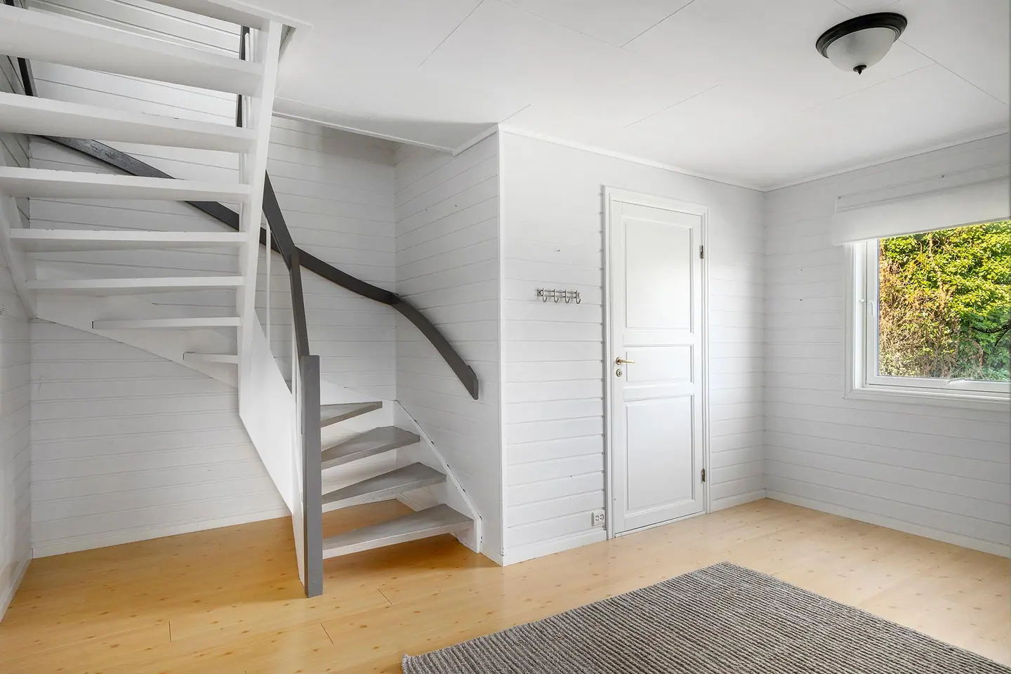 Hall med malt trepanel på veggene og trappeløp opp til andre etasje.
